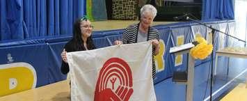 karen Kirkwood-White hold the United Way flag with new Chatham-Kent branch campaign chair Caterina Dawson at a ceremony at École secondaire catholique de Pain Court. June 15, 2018. (Photo by Greg Higgins)
