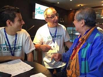 Tom Dalios with Dalios Hearing and Denture Clinic (centre) fitting new hearing aids at the Rogers Centre, October 6, 2016 (Photo courtesy of Dalios Hearing and Denture Clinic)
