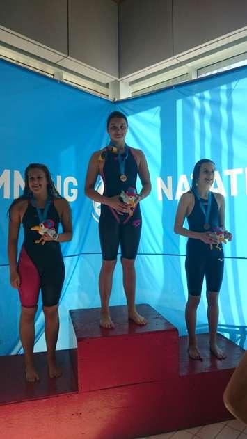 Chatham Y Pool Shark Madison Broad (centre) receives gold medal at Canadian Age Group Championships (Photo courtesy of Bailey Salmon Moskal)